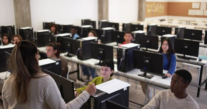 Mature teacher working with students inside computer classroom at school college