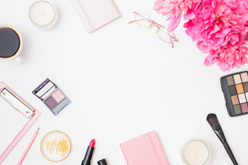 Fashion blogger workspace with notepad, glasses, cup of coffee, pencil and pink peonies on a white table. Flat lay banner or shop header with makeup cosmetic products