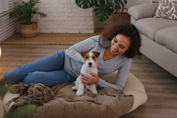 Portrait of young beautiful black woman with her adorable wire haired Jack Russel terrier puppy at home. Loving girl with rough coated pup having fun. Background, close up, copy space.