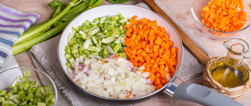 Preparation of the Italian classic base for dishes - soffritto. Finely chopped onions, carrots and celery in a skillet on the table with ingredients. Background for Italian cuisine - soffritto.