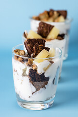 Healty Desserts with Yogurt Cream Granola Fruits and Chocolate Cookies with Oatmeal Served in Glasses Diet Tasty Desserts Blue Background Vertical