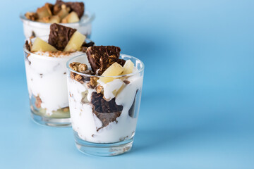 Healty Desserts with Yogurt Cream Granola Fruits and Chocolate Cookies with Oatmeal Served in Glasses Diet Tasty Desserts Blue Background Copy Space