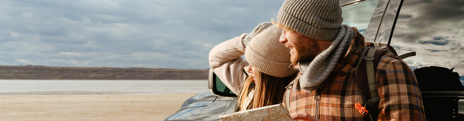 White happy couple talking and examining paper map during car trip