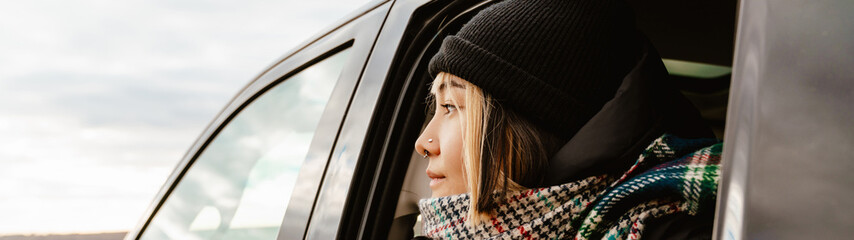 Asian woman wearing hat looking out window during car trip