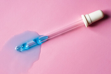 Blue drops of transparent liquid near pipette on pink background