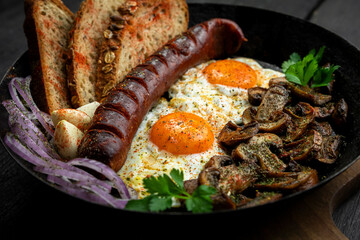 Fried eggs and sausage with mushrooms served in cast iron pan in the kitchen