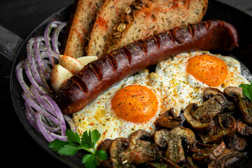 Fried eggs and sausage with mushrooms served in cast iron pan in the kitchen