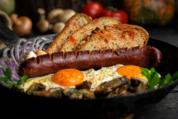 Sausage and fried eggs with toasted bread, mushrooms and onions served in cast iron dish. Selective focus on the sausage