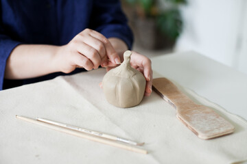 woman sculpting a pumpkin out of clay with tools - hobby and DIY project at home hands close up