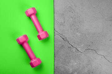 Top view of  green sport mat and pink dumbbells on marble grey background or set for pilates or fitness practice with copy space.