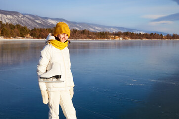 Portrait of a smiling female athlete with figure skates on the background of frozen Lake Baikal. Active recreation, unity with nature, outdoor sports, natural background. 
