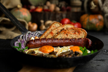 Sausage and fried eggs with toasted bread, mushrooms and onions served in cast iron dish. Selective focus on the sausage