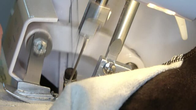 Close-up of the sewing foot and needle of a sewing machine sewing a garment.