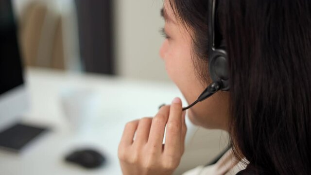 Close up smiley asian business woman receptionist wear headphone video conference calling on computer talk by webcam in online chat, customer support service concept. 