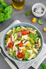 Healthy vegan pasta salad with tomatoes, cucumbers, red onions and arugula in a bowl on a dark gray background. Copy space.