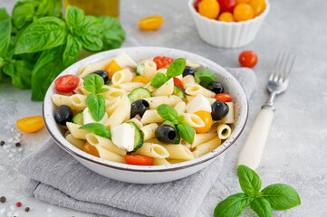 Healthy pasta salad with tomatoes, cucumbers, red onions, olives and cheese in a bowl on a gray background. Copy space.