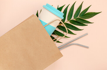 Paper bag with bamboo cup and reusable drinking straws on pink background. Mockup, top view. Zero waste concept