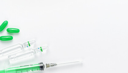 Syringe, ampules and green pills on white background. Medical treatment and vaccination concept. Copy space, overhead