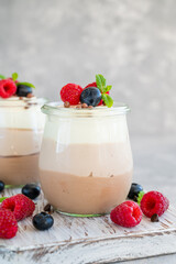 Dessert three chocolate in a glass jar with fresh blueberries, raspberries and blackberries on top on a gray concrete background. Dessert with three layers of different taste. Copy space.