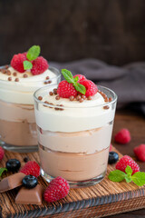 Dessert three chocolate in a glass jar with fresh blueberries, raspberries and blackberries on top on a dark wooden background. Dessert with three layers of different taste. Copy space.