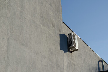 External air conditioner unit on gray wall.
