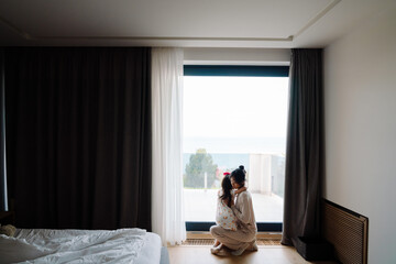Naklejka premium Asian woman and her daughter looking out window while together