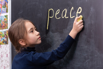 The girl writes the word peace on the blackboard..