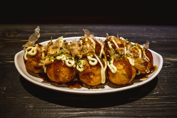 Selective focus at Takoyaki or Japanese octopus balls, serve on white plate on wooden counter in...