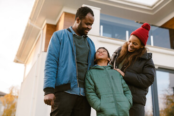 Fototapeta premium Black family smiling and talking while standing by house