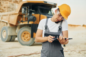 In glasses and hard hat. Worker in professional uniform is on the borrow pit at daytime