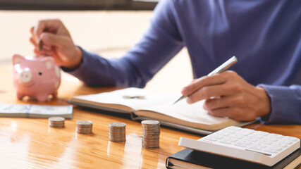 saving concept the man writing down his income and counting some money as a saving-up part on his notebook while dropping a coin into the piggy bank