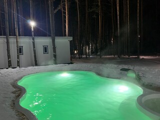 Thermae - a heated outdoor pool illuminated in green at night in the snow with steam coming from the pool in winter
