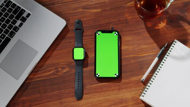 Smartwatch and phone with green screen top view. Smartphone touchpad with chroma key close-up, laptop computer on table. 
