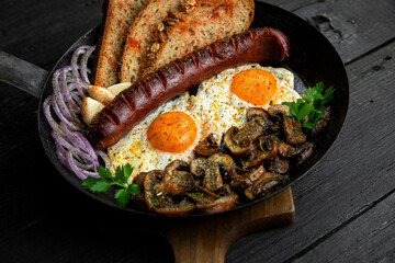 Fried eggs and sausage with mushrooms served in cast iron pan in the kitchen