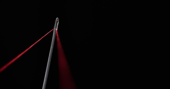 Red thread going through needle eye, closeup