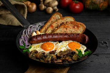 Fried eggs and sausage with mushrooms served in cast iron pan in the kitchen