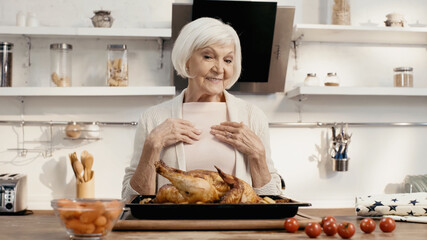 joyful woman looking at delicious turkey near fresh cherry tomatoes and carrots in kitchen.