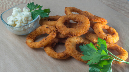 A close-up image for the bar menu. Juicy crispy onion rings lie on a crafting background with parsley leaves.