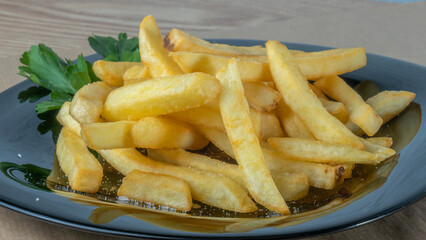 French fries on black dish on parchment background. Tasty golden french fries on a plate.