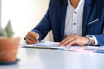 Asian male finance staff is calculating by using a calculator. Investment results to report to his boss at the meeting. On the table in the office, the concept of calculating investment results