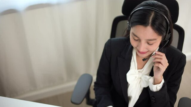 Top view smiley asian business woman receptionist wear headphone video conference calling on computer talk by webcam in online chat, customer support service. 