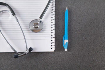 Stethoscope, notebook and pen on gray background.