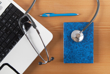 Stethoscope, computer, notebook and pen on wooden background. Doctors desk.