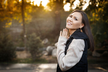 Smiling young woman on the right side of the photo stands outdoors in autumn in a warm sweater and...