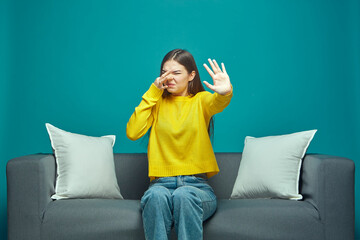 Bad smell. Young girl pinch nose showing stop gesture, feel disgust sitting on sofa. Stench,...