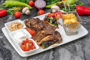 Grilled lamb chops with french fries and appetizers on a white porcelain plate