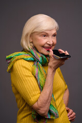 Senior woman in yellow shirt and with a green scarf recording a voice message