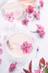 Obraz na płótnie Canvas Romantic spingtime floral background with rose light sparkling wine in the two coupes glasses with beautiful soft pink flowers, selective focus