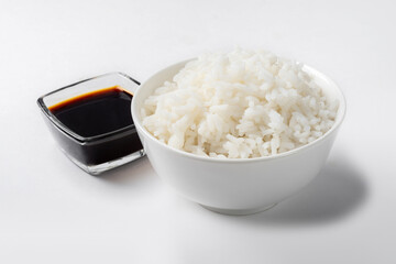 Long-grain boiled rice in a white cup on a white background with soy sauce