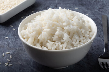 Long-grain boiled rice in a white cup on a dark blue background